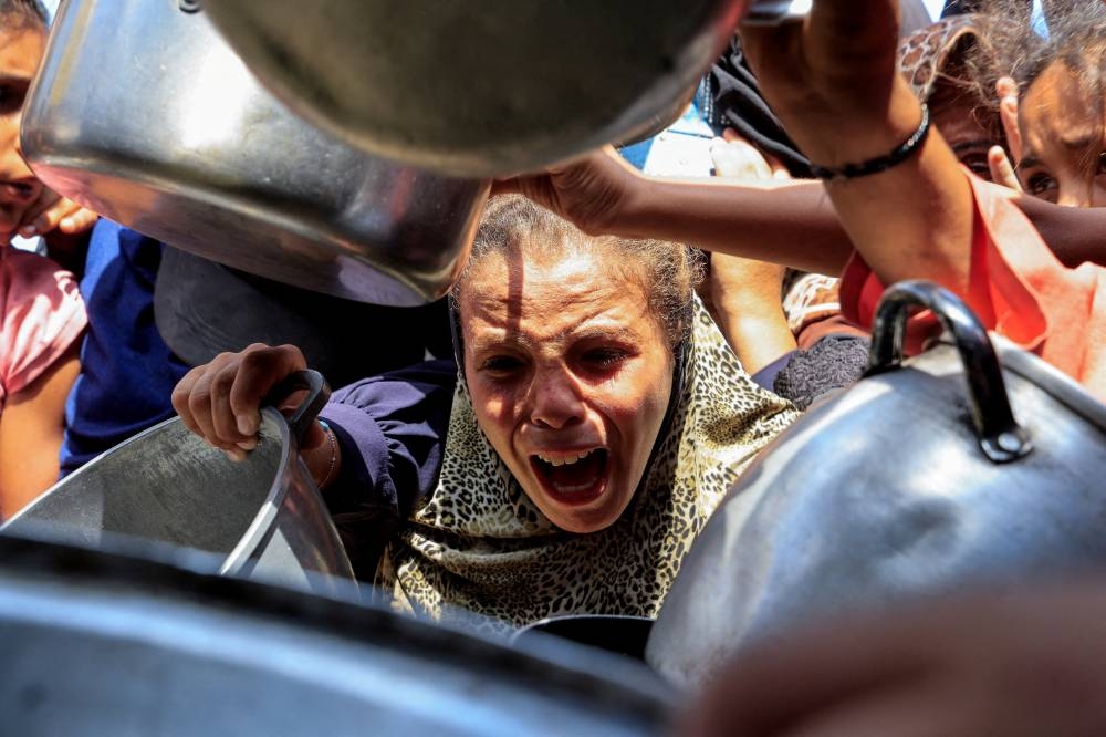 A Palestinian reacts while waiting to receive food from a charity kitchen, in Khan Younis, southern Gaza Strip, August 21, 2025. REUTERS