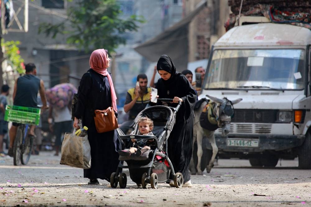 A woman pushes a stroller as Palestinians flee with their belongings the Abu Iskandar neighborhood of northern Gaza City on August 22, 2025. (AFP)