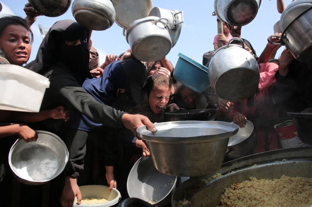 Palestinian women and children hold out their empty pots in front of a charity kitchen in Khan Yunis in the southern Gaza Strip on August 21, 2025. (AFP)