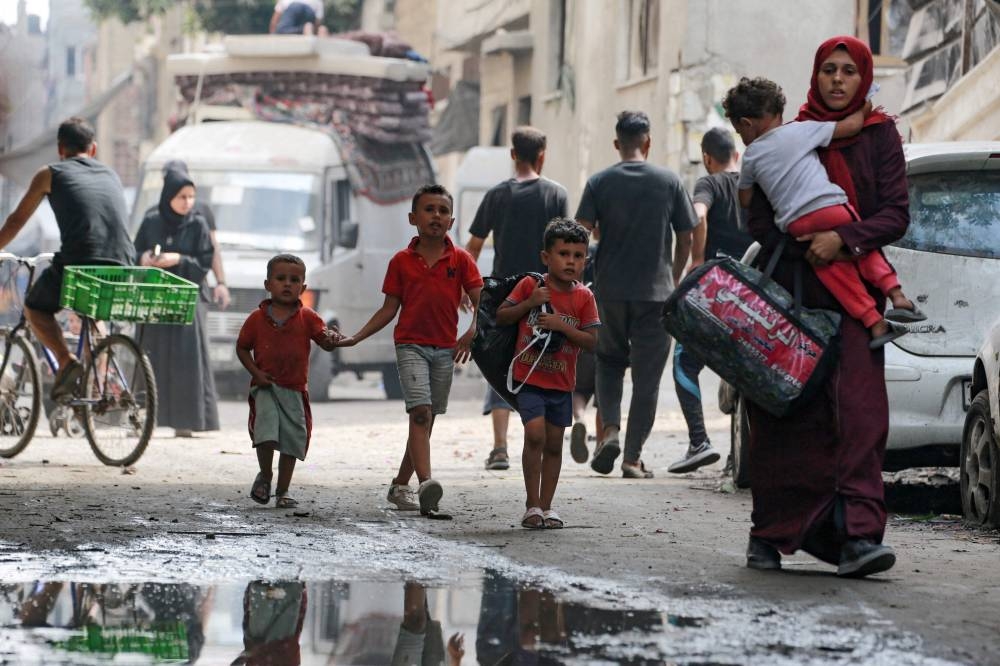 A Palestinian woman carries a child as she flees with others the Abu Iskandar neighborhood of northern Gaza City on August 22, 2025. (AFP)
