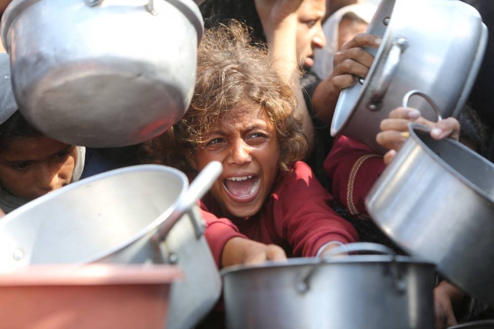 A child reacts surrounded by pots as Palestinians wait to receive food from a charity kitchen in Khan Younis, southern Gaza Strip, on Thursday. REUTERS