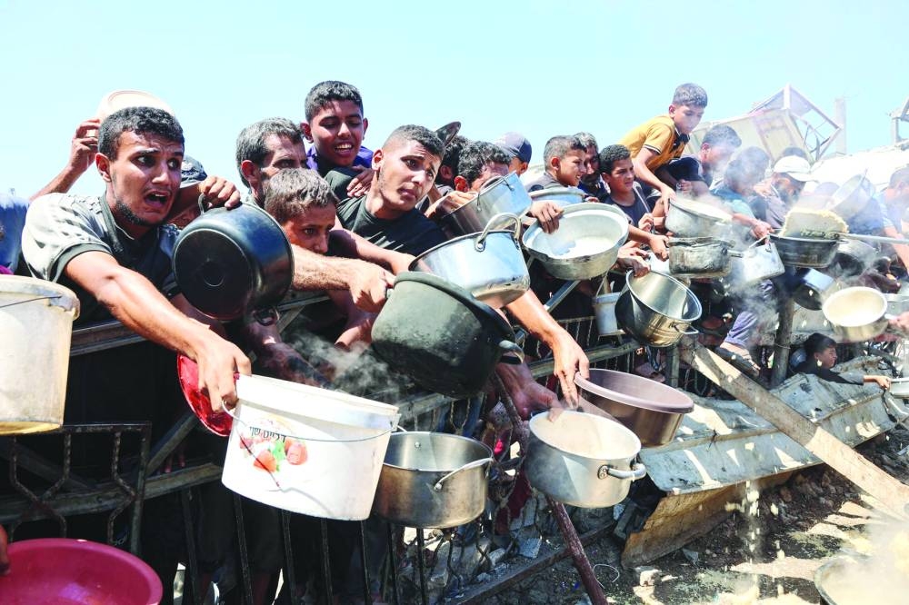 TOPSHOT - Palestinian men and boys extend their empty pots to receive cooked rice from charity kitchen in Gaza City on August 23, 2025. The United Nations officially declared a famine in Gaza on August 22, blaming "systematic obstruction" of aid by Israel during more than 22 months of war, with Prime Minister Benjamin Netanyahu swiftly dismissing the findings. (Photo by Omar AL-QATTAA / AFP)