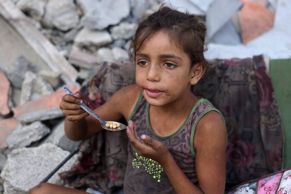 A displaced Palestinian girl eats chickpeas as she sits amid the destruction in Saftawi neighbourhood, west of Jabalia in the northern Gaza Strip, on Sunday. AFP