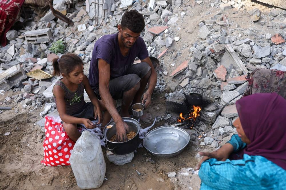 A displaced Palestinian man and his family warm up chickpeas as they sit amid the destruction in Saftawi neighbourhood, west of Jabalia in the northern Gaza Strip, on Sunday. AFP
