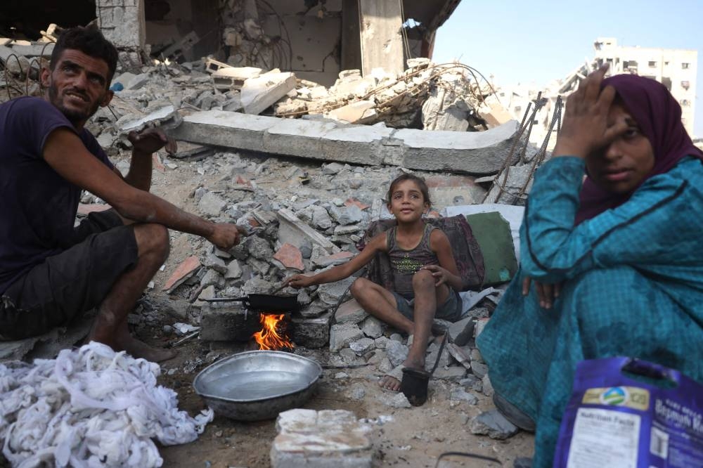 A displaced Palestinian man and his family warm up chickpeas as they sit amid the destruction in Saftawi neighbourhood, west of Jabalia in the northern Gaza Strip, (AFP)