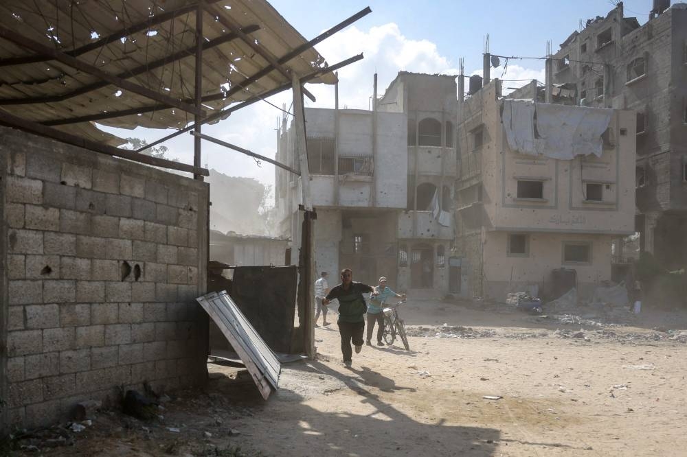 Palestinians run for cover following an explosion in the Saftawi neighborhood, west of Jabalia in the northern Gaza Strip on August 25, 2025, (AFP)