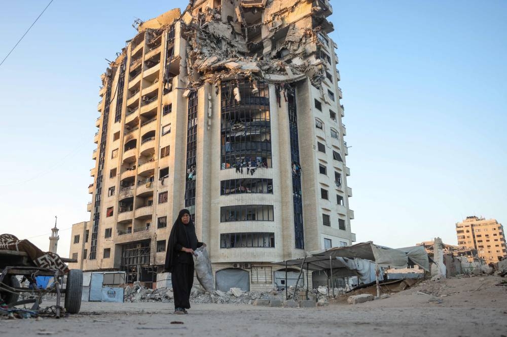 A Palestinian woman walks past a heavily damaged building in Gaza City on August 29, 2025. (AFP)