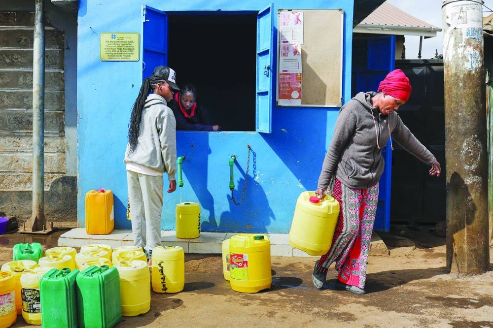 Margaret John (right), 50, collects jerrycans of clean piped water from a distribution point after redeeming digital points earned from delivering plastic waste to a Human Needs Project (HNP) collection point in the Kibera informal settlement of Nairobi.
