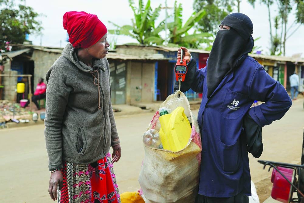 Margaret John, 50, (L) delivers a sack of plastic waste collected in her neighborhood to a Human Needs Project (HNP) official at a collection point in the Kibera informal settlement of Nairobi, on August 11, 2025. Kenya's largest informal settlement water and sanitation have remained scarce and costly, often controlled by cartels who charge residents prices beyond their means. The Human Needs Project (HNP) seeks to mitigate that: residents in Kibera can trade discarded plastic for "green points", or credits, that they can then redeem for services such as drinking water, toilets, showers, laundries, and even meals. (AFP)