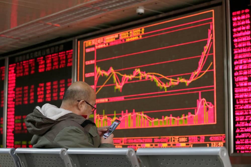 An investor looks at his mobile phone in front of a board showing stock information at a brokerage office in Beijing (file).