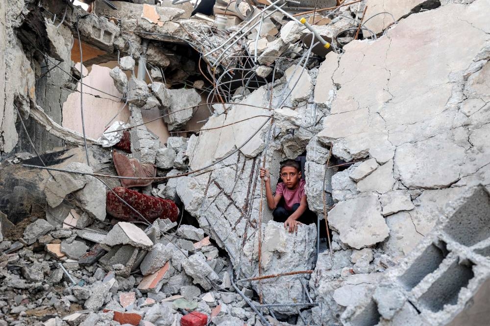A boy climbs from out of the rubble of a collapsed building that was hit by bombardment in the Nuseirat camp for Palestinian refugees in the central Gaza Strip Saturday. (AFP)