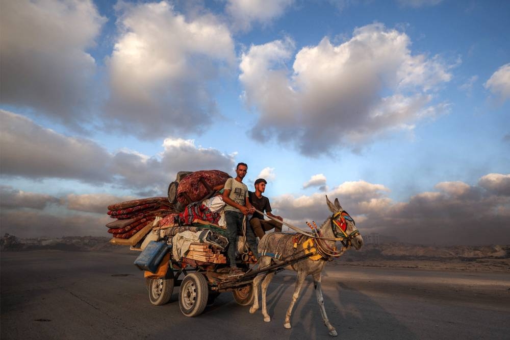 Men ride a donkey-drawn cart loaded with a cistern, mattresses, beddings, and packed tents moving along the coastal road as people evacuate southbound from Gaza City on Tuesday. AFP