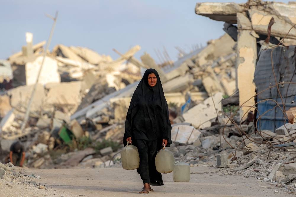 A woman walks with jerrycans loaded with water past the rubble of destroyed buildings in Gaza City on Tuesday. AFP