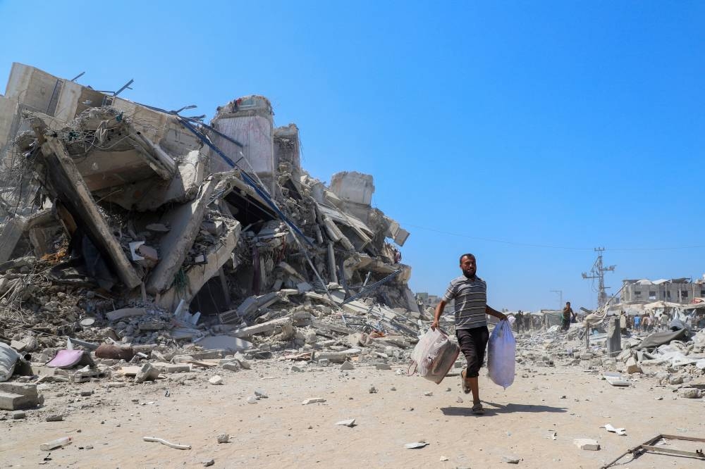 A Palestinian man runs with belongings next to rubble after a building was hit by an Israeli air strike, in Gaza City, September 5, 2025. REUTERS