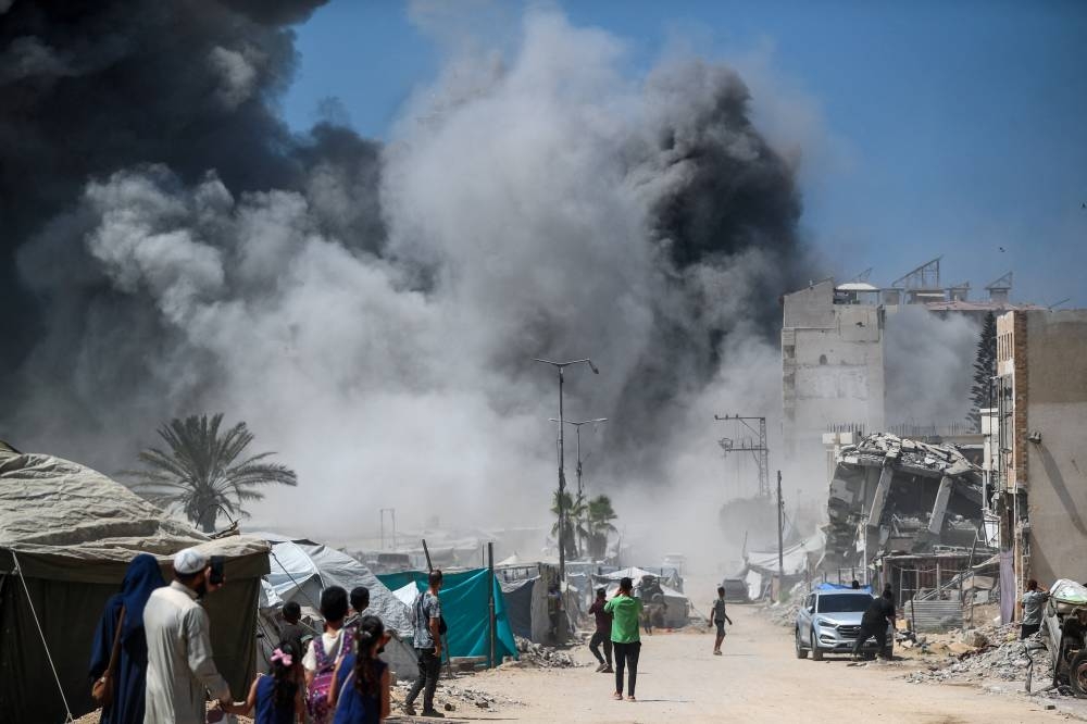 Palestinians watch as smoke rises after a building was hit by an Israeli air strike, in Gaza City