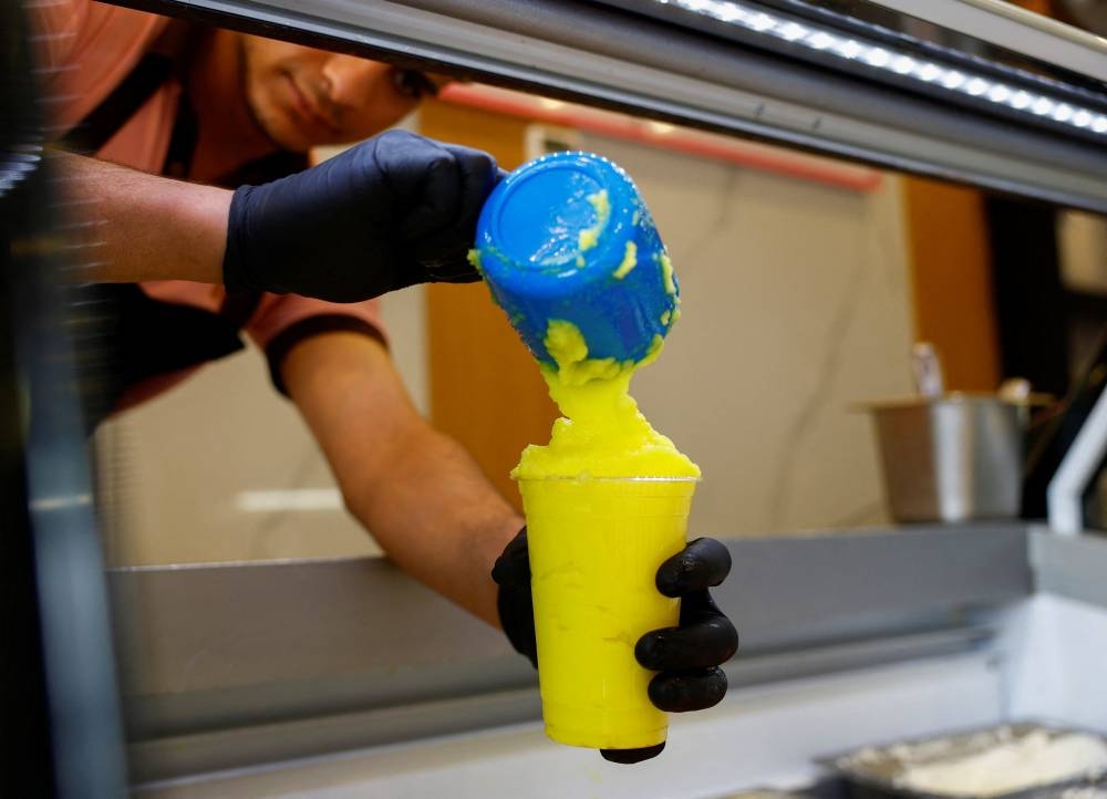 A worker fills a cup of "Barrad", a traditional Palestinian slushy drink with citrus flavours, at a newly opened branch of an ice cream shop that was partially destroyed in Gaza during the ongoing conflict between Israel and Hamas, in Ajman, United Arab Emirates, August 19, 2025. REUTERS/Raghed Wake