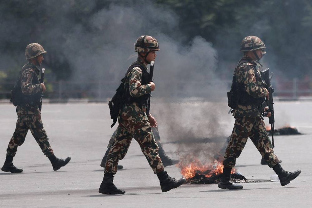 Soldiers armed with assault rifles walk past a road near the burning Nepali Congress Party office during a protest to condemn the police's deadly crackdown on demonstrators in Kathmandu on September 9, 2025 (AFP)