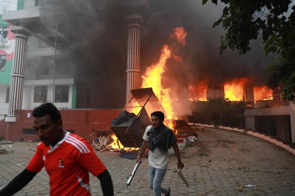 Demonstrators walk past flames outside the burning Nepali Congress Party office during a protest to condemn the police's deadly crackdown on demonstrators in Kathmandu on September 9, 2025 (AFP)
