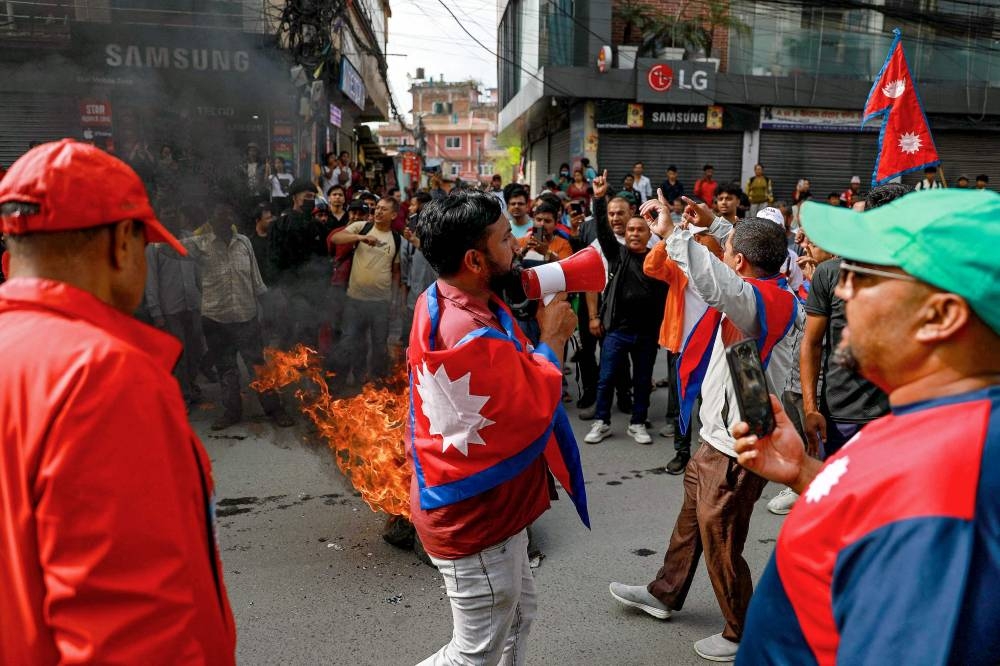 A man draped in Nepal's national flag uses a loadspeaker as tyres are burnt during a demonstration to condemn the police's deadly crackdown on protesters in Kathmandu on September 9, 2025, (AFP)