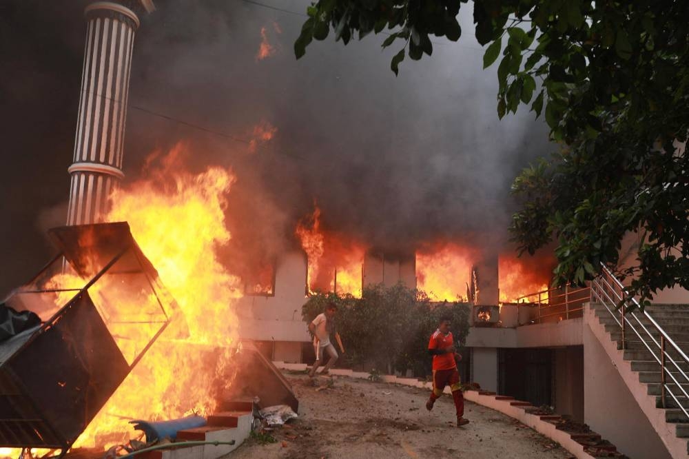 Demonstrators run past flames outside the burning Nepali Congress Party office during a protest to condemn the police's deadly crackdown on demonstrators in Kathmandu on September 9, 2025 (AFP)