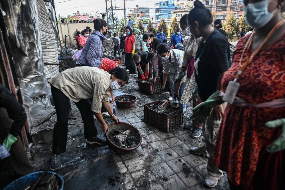 Local residents clean up the rubble of a burnt supermarket after it was set ablaze during protests in Kathmandu, on Saturday. AFP