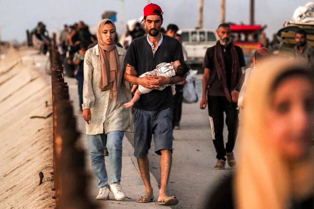 A couple with an infant walk with other displaced Palestinians evacuating southbound from Gaza City along the coastal road in Nuseirat in the central Gaza Strip Saturday.