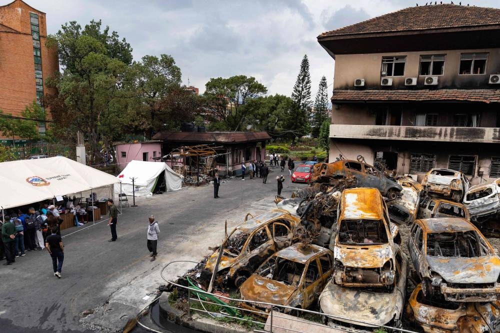 Court personnel gather under makeshift tents beside heaps of charred vehicles at the torched Supreme Court premises in Kathmandu, on Sunday. AFP