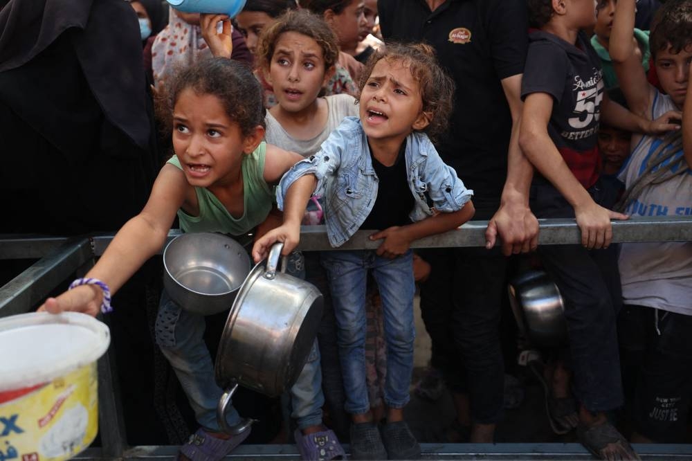 Palestinian children hold out their pans in front of a charity kitchen in the Nuseirat refugee camp in the central Gaza Strip, on Sunday. AFP
