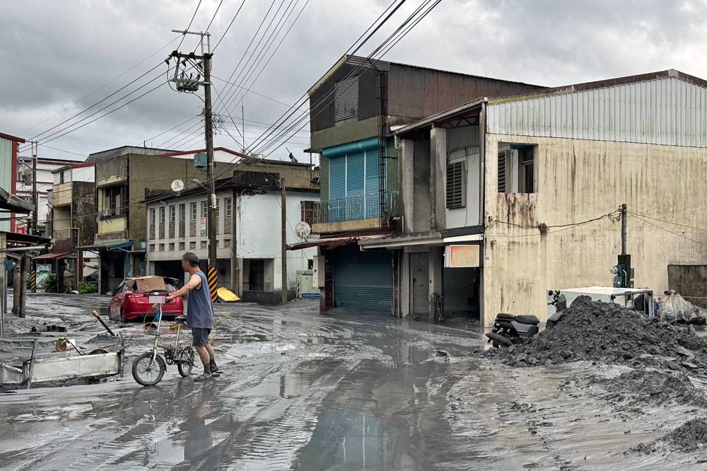 A resident holds a bicycle along a street covered with mud in Hualien on September 24, 2025, following the bursting of a barrier lake. The bursting of the barrier lake in Taiwan killed at least 14 people, regional officials said on September 24 after Super Typhoon Ragasa pounded the island with torrential rains. (AFP)
