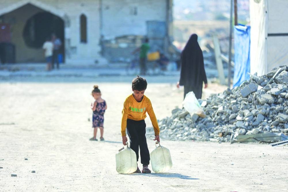 A Palestinian boy displaced by the conflict carries water containers in northwestern Khan Younis, yesterday