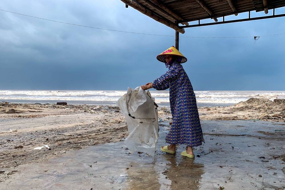 A woman wearing a raincoat collects a plastic bag near a beach as Typhoon Bualoi nears, in Nghe An province, Vietnam, on Sunday. REUTERS