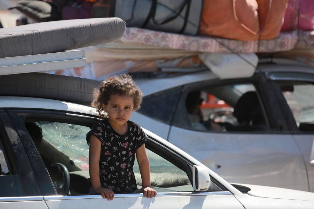 A girl looks out a car window while Palestinians carrying belongings arrive on a coastal path northwest of Nuseirat refugee camp as they are displaced southward from Wadi Gaza following an Israeli announcement of closing Al-Rashid road towards the north of the besieged Gaza Strip, on Wednesday. AFP