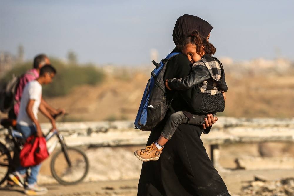 A Palestinian woman carrying her child walks along the so-called "Netzarim corridor" as she makes her way to Gaza City from Nuseirat in the central Gaza Strip on October 11, 2025. Israel declared a ceasefire in Gaza and began to pull back its forces on October 10, as tens of thousands of exhausted Palestinians made their way back to their devastated homes. (AFP)