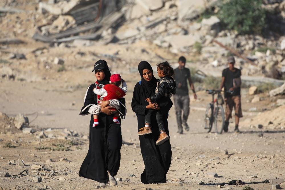 Palestinian women carrying their children walk with others along the so-called "Netzarim corridor" as they make her way to Gaza City from Nuseirat in the central Gaza Strip on October 11, 2025. Israel declared a ceasefire in Gaza and began to pull back its forces on October 10, as tens of thousands of exhausted Palestinians made their way back to their devastated homes. (AFP)