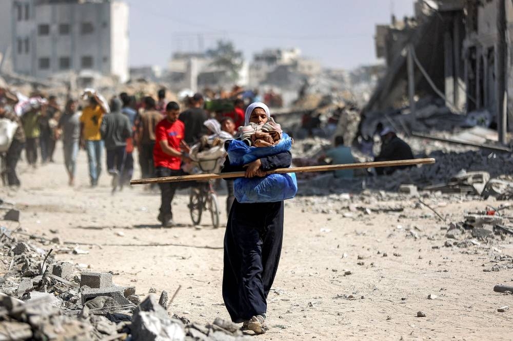 A woman walks with a package and a long wooden beam along a destroyed road past heavily-damaged buildings in the centre of Khan Yunis in the southern Gaza Strip on October 10, 2025, as displaced people return to their homes after Israeli forces' withdrawal. Gaza's civil defence agency said on October 10 that Israeli forces have begun pulling back from parts of the territory, particularly in Gaza City and Khan Yunis.  (AFP)