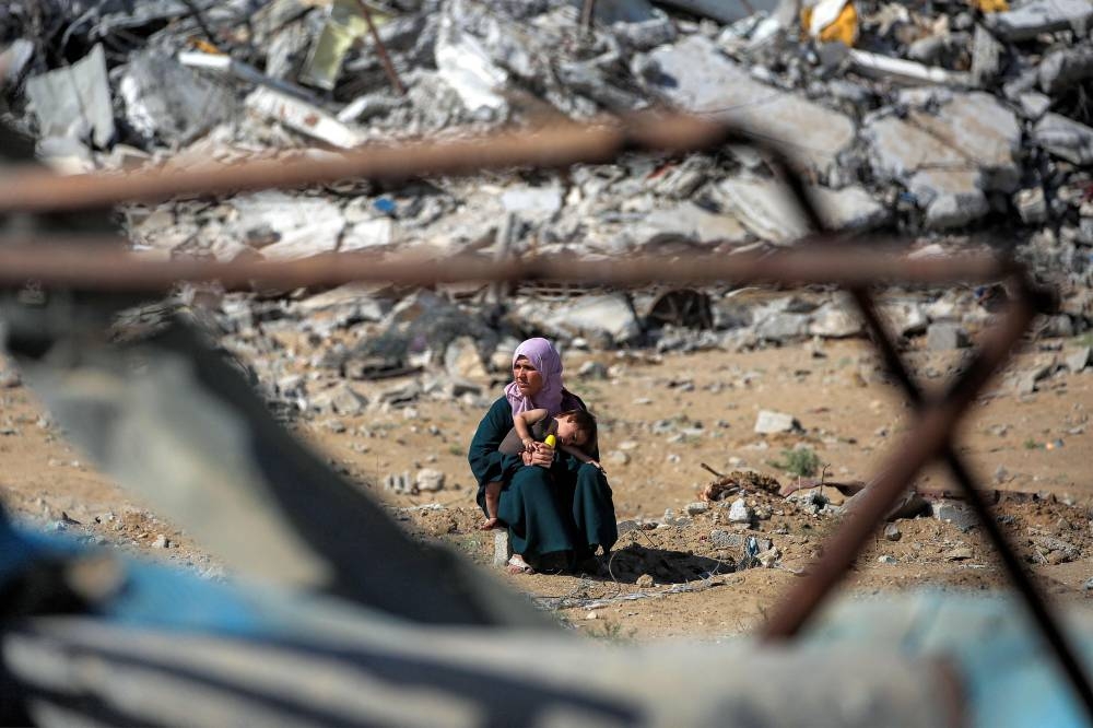 A woman sits with a child before a mound of rubble on the road to Gaza City near Nuseirat in the central Gaza Strip on October 10, 2025. Gaza's civil defence agency said on October 10 that Israeli forces have begun pulling back from parts of the territory, particularly in Gaza City and Khan Yunis. (AFP)