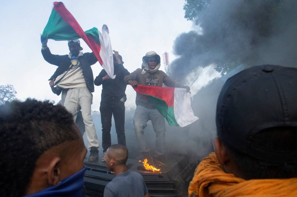 Protesters hold national flags of Madagascar as they chant atop a burning armoured riot police vehicle during a nationwide youth-led protest over frequent power outages and water shortages, in Antananarivo, Madagascar, on Saturday. REUTERS