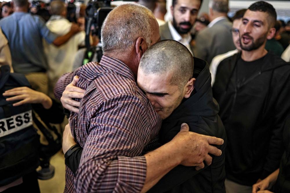 One (R) of the Palestinian prisoners, who was released in a prisoner-hostage swap and ceasefire deal between Israel and Hamas, is embraced by his father upon arrival by bus at Ramallah Cultural Centre in Ramallah in the occupied West Bank, on Monday. AFP