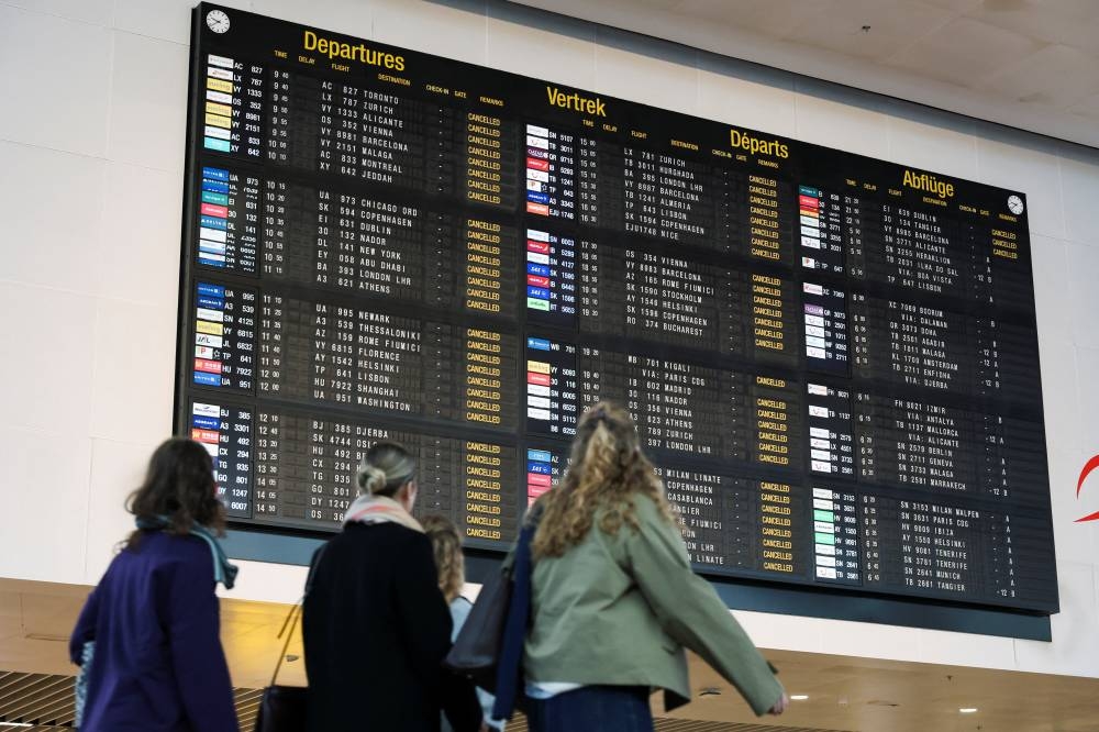 Passengers look at a board displaying information on cancelled flights, during a nationwide strike against the government's reform plans, at Brussels Airport in Zaventem near Brussels, Belgium October 14, 2025.  REUTERS