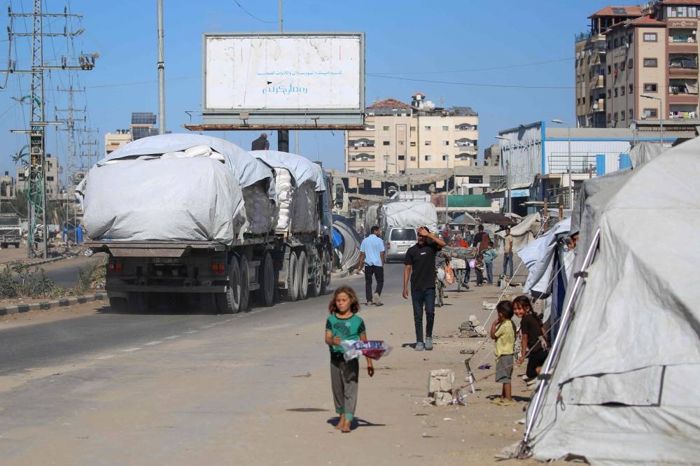 Trucks carrying aid which entered Gaza through the Karm Abu Salem crossing, drive past displacement tents at the Nuseirat refugee camp in the central Gaza Strip, on Tuesday. AFP