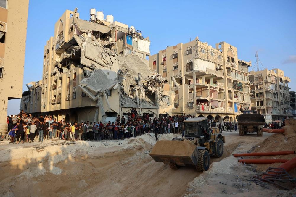 People watch as Palestinians use an excavator to dig deep into the ground, reportedly searching for bodies in Khan Yunis in the southern Gaza Strip Friday.