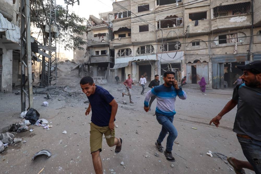 People run for cover following an Israeli strike that targeted a building in the Bureij camp for Palestinian refugees in the central Gaza Strip on Sunday. AFP