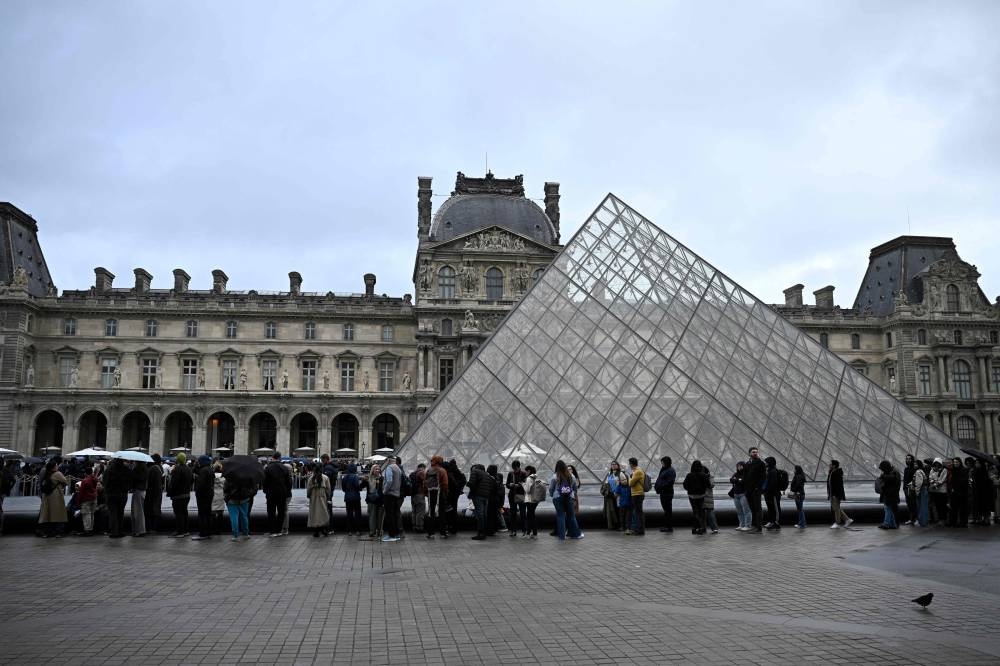 People queue in the Louvre pyramid courtyard moments before the announcement the museum will remain closed for a second day running after thieves stole crown jewels from the museum in Paris a day earlier, in Paris on Monday. AFP
