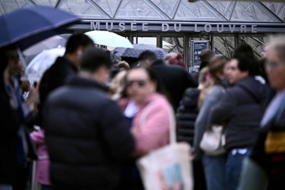 People queue in the Louvre pyramid courtyard moments before the announcement the museum will remain closed for a second day running after thieves stole crown jewels from the museum in Paris a day earlier, in Paris on Monday. AFP