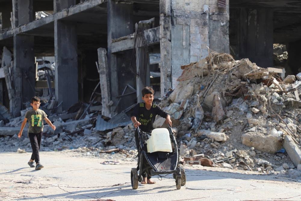 Displaced Palestinian children walk, as one of them moves a cart loaded with water containers, amid a ceasefire between Israel and Hamas, in Gaza City, on Saturday. REUTERS