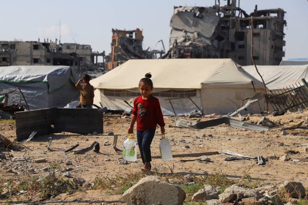 A displaced Palestinian girl carries water containers near tents, amid a ceasefire between Israel and Hamas, in Gaza City, on Saturday. REUTERS