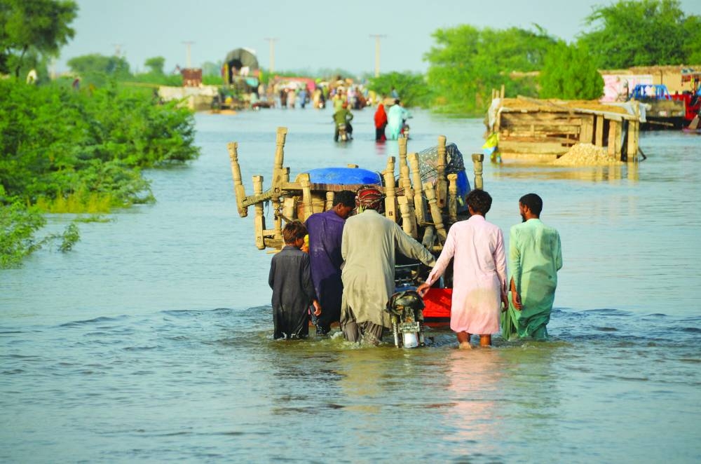 
Men walk along a flooded road with their belongings, following rains and floods during the monsoon season in Suhbatpur, Pakistan. (Reuters/File photo) 