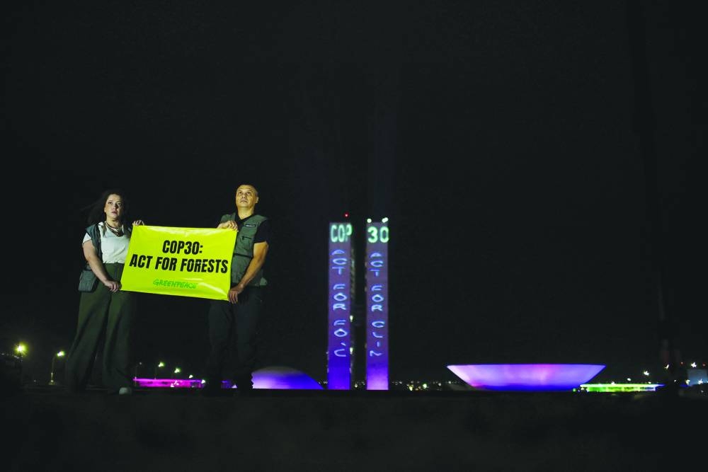 Greenpeace activists hold a sign reading ‘Cop 30: Act for forests’, as they project slogans onto Brazil’s National Congress to urge COP30 negotiators to protect forests and the Amazon as part of efforts to combat the climate crisis, outside Brazil’s National Congress, in Brasilia, Brazil, on October 11, 2025.