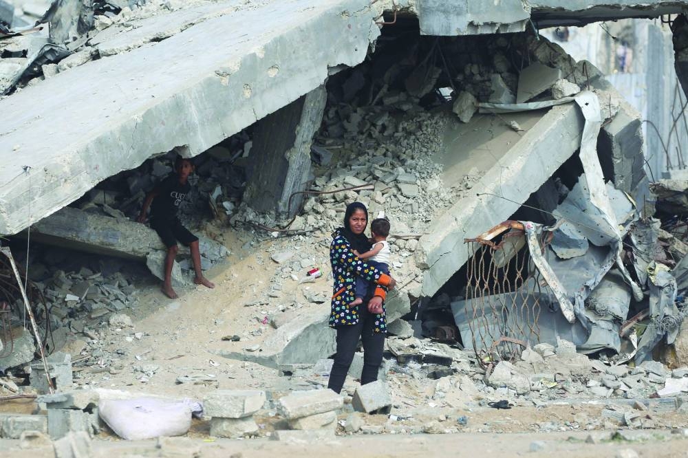 A Palestinian woman carries her child past destroyed buildings along a road close to the Nuseirat refugee camp in the central Gaza Strip, Sunday.