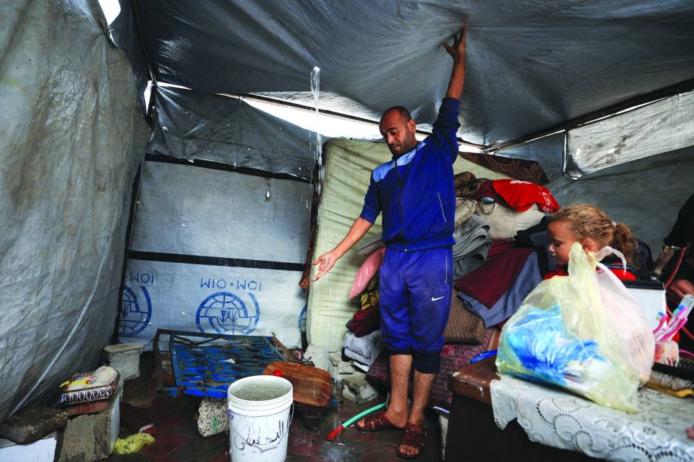 A Palestinian man removes water from the roof top of a tent on a rainy day, during a ceasefire between Israel and Hamas, in Gaza City.